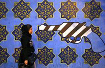 DATEI - Eine iranische Frau geht am Samstag, 2\. November 2013, in Teheran, Iran, an einem gegen die USA gerichteten Wandgemälde vorbei, das an die Wand der ehemaligen US-Botschaft gemalt wurde.
