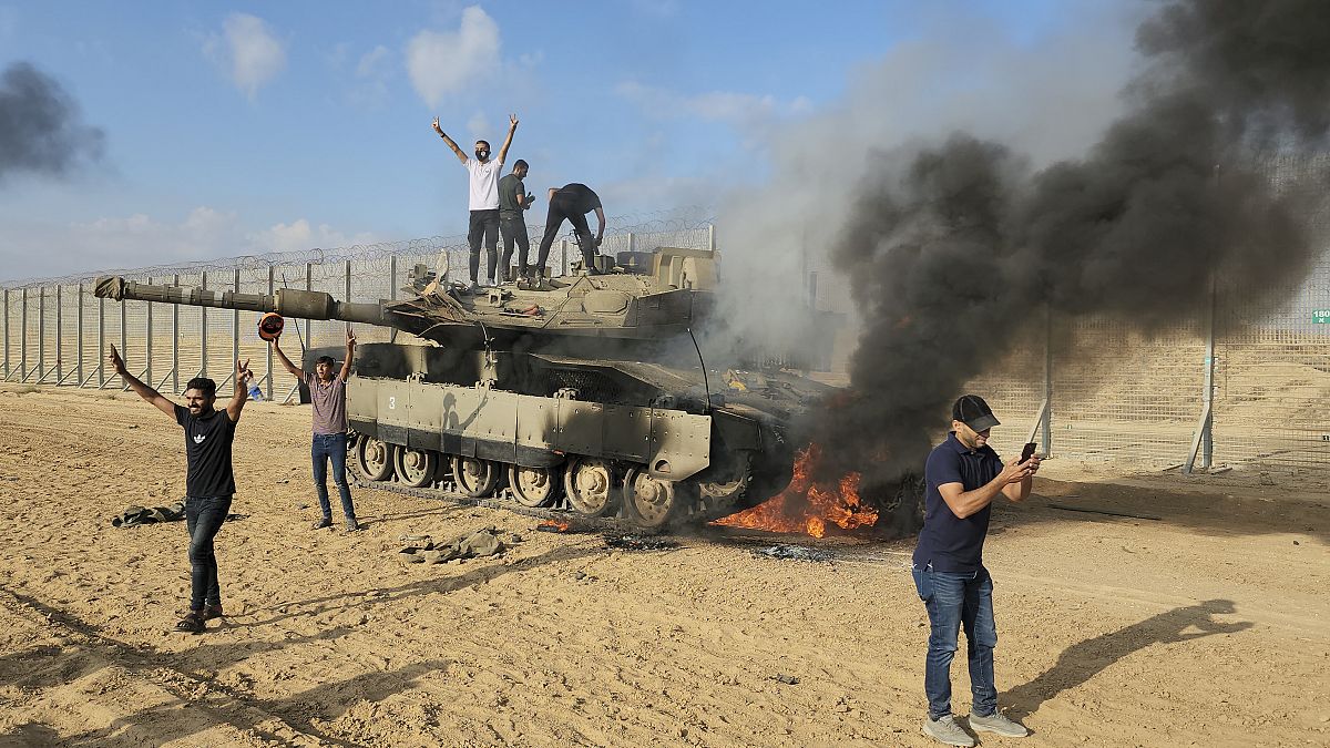 Palestinians celebrate by a destroyed Israeli tank at the Gaza Strip fence east of Khan Younis on Saturday