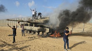 Palestinians celebrate by a destroyed Israeli tank at the Gaza Strip fence east of Khan Younis on Saturday