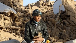Una víctima del terremoto de este sábado en Afganistán sujeta a su gato frente a un montón de escombros. 