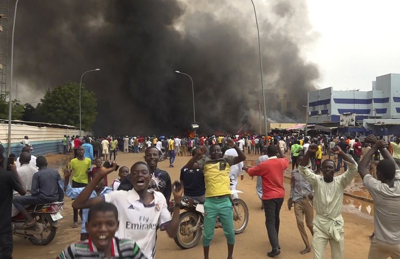 FILE - With the headquarters of the ruling party burning in the back, supporters of Niger's ruling junta demonstrate in Niamey, Niger, on July 27, 2023.