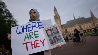 Manifestante à porta do TIJ com cartaz evocando pessoas desaparecidas na Síria