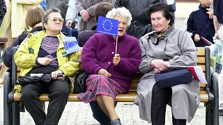 Women with EU and Polish flags sit on a market square bench in the southern Poland town of Prudnik Sunday April 27, 2003. 