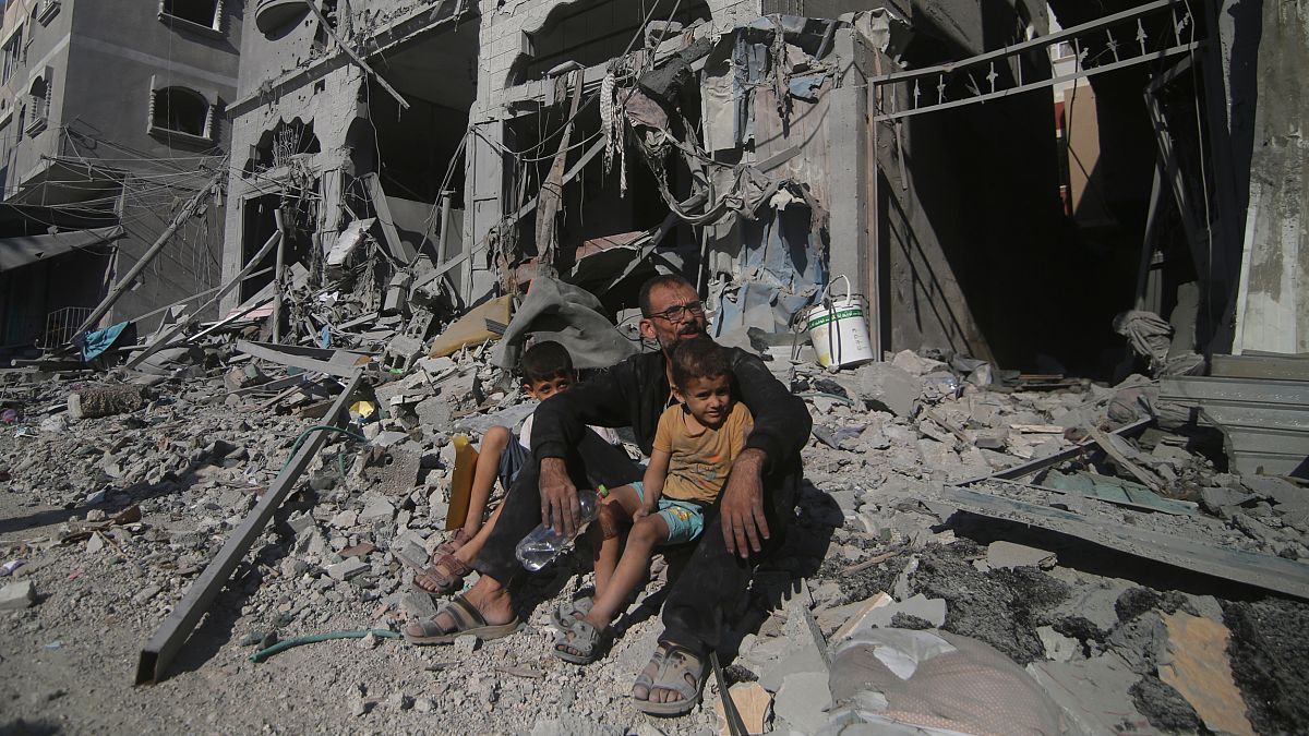 Palestinianos sentados hoje numa rua destruída após um bombardamento israelita