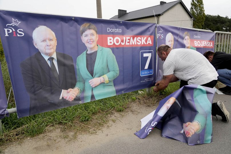 A man puts up election banners for a candidate of the ruling PiS party together with party leader Jaroslaw Kaczynski in Czosnow near Warsaw, October 2023