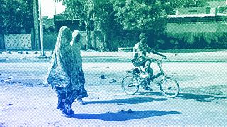 Two women walk as a boy cycles in the streets of Niamey, August 2023