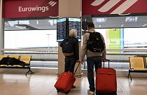 Reisende vor einem Bildschirm mit Flugdaten am Flughafen Köln-Bonn, Deutschland, April 2023.