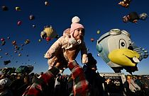 Baby Clarissa wird von ihrem Vater in die Luft gehoben, während Heißluftballons bei der Albuquerque International Balloon Fiesta in Albuquerque aufsteigen.