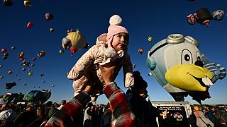 Baby Clarissa wird von ihrem Vater in die Luft gehoben, während Heißluftballons bei der Albuquerque International Balloon Fiesta in Albuquerque aufsteigen.
