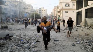 A Palestinian carrying a child runs following an Israeli strike in the southern Gaza Strip on Saturday as fighting between Israel and Hamas continues for an eighth day