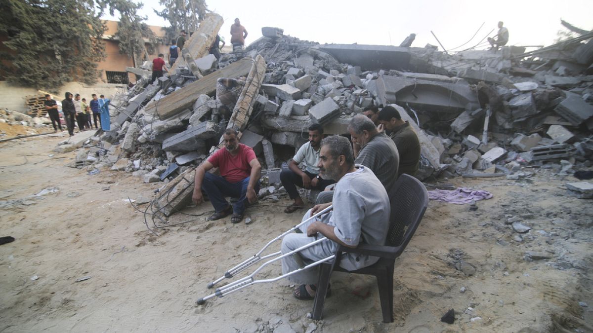 Palestinos sentados junto al edificio destruido en un ataque aéreo israelí en Rafah, Franja de Gaza, sábado 14 de octubre de 2023.