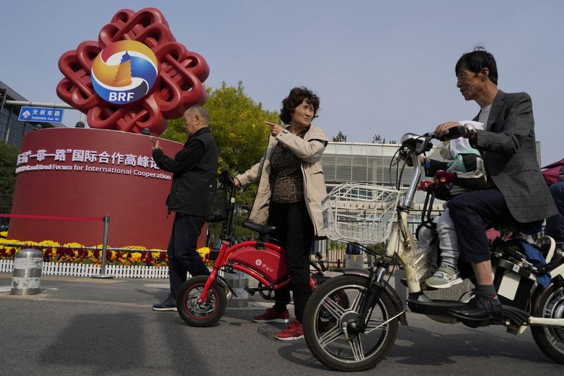 Residents pass by the logo for the Belt and Road Forum outside the China National Convention Center in Beijing, October 2023