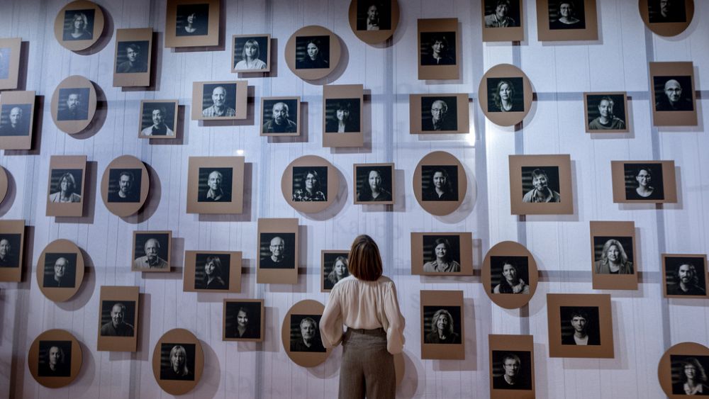 Жена стои пред стена със снимки на словенски автори в