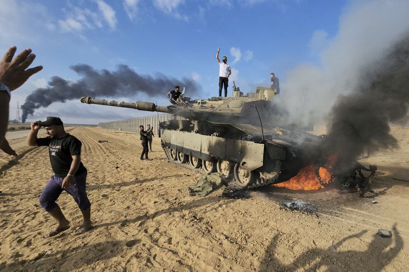 Palestinians celebrate by a destroyed Israeli tank at the border fence between Israel and the Gaza Strip, 7 October 2023