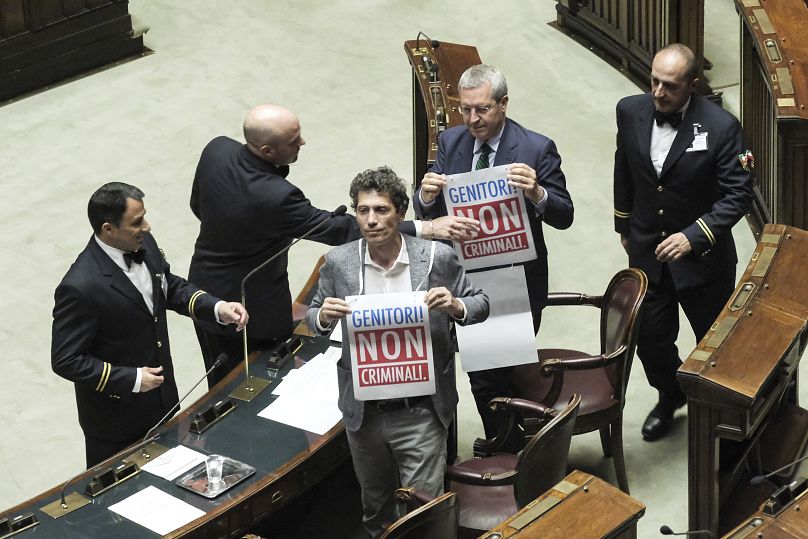 +Europa's lawmakers Riccardo Magi, and Benedetto Della Vedova hold placards reading in Italian: "Parents not criminals" in Lower Chamber during surrogacy debate