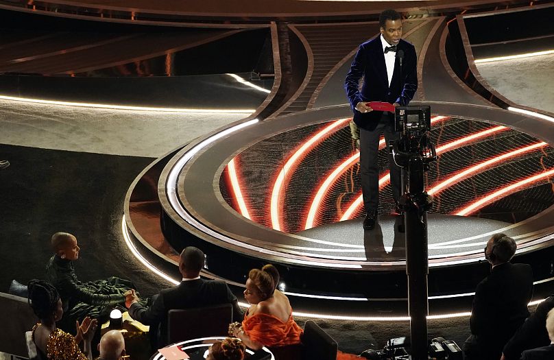 At the 2022 Oscars on 27 March, presenter Chris Rock seaks onstage as Jada Pinkett Smith and Will Smith, who would later confront him, observed from their seats.