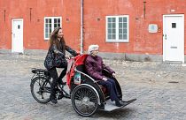Um voluntário e membro da associação "Un Vélo Pour Tous" transporta uma senhora idosa numa bicicleta de carga, a 5 de maio de 2019, no centro de Copenhaga.