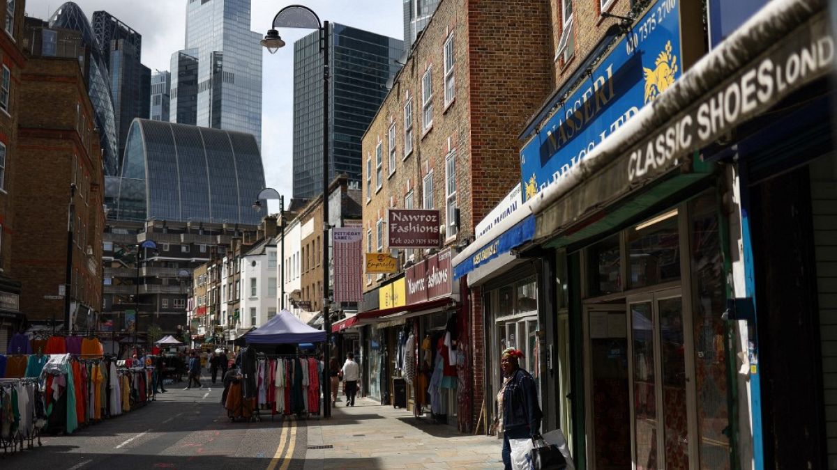 A shopper leaves a shop in Petticoat Lane Market, against the backdrop of The City of London financial district in London on August 11, 2023. 