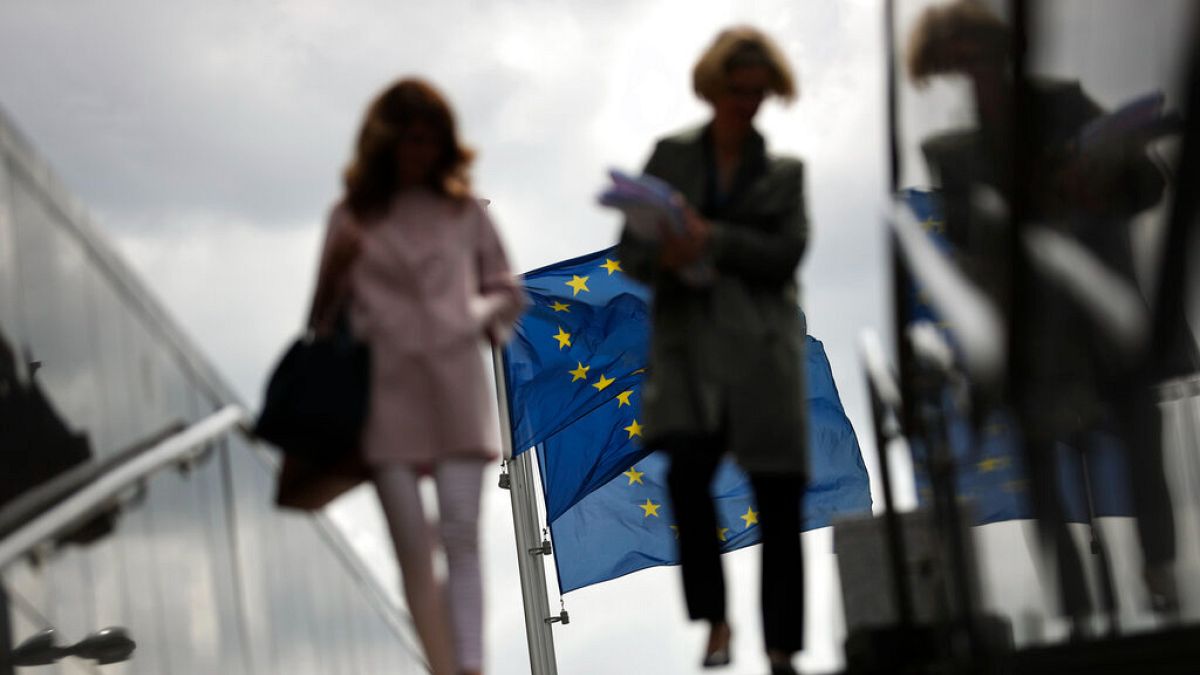 FILE - Due donne camminano vicino alle bandiere dell'UE fuori dalla sede della Commissione europea a Bruxelles, lunedì 27 maggio 2019.