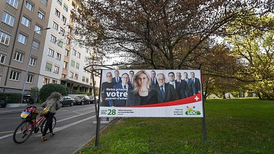 A cyclist pushes her bike past an electoral poster of candidates of Swiss People's Party (SVP UDC) in Aarberg, canton of Bern