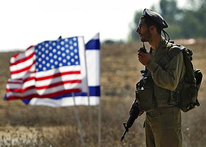 Demir Kubbe hava savunma sistemi yanındaki Amerikan ve İsrail bayraklarının önünde duran bir İsrail askeri (arşiv)