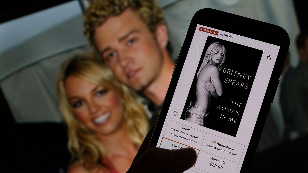 ) This illustration image taken on October 21, 2023 shows the cover of Britney Spears' book "The Woman in Me" from an online retailer in front of a picture of Britney Spears.