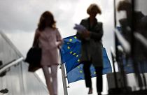 Two women walk near EU flags outside the European Commission headquarters in Brussels