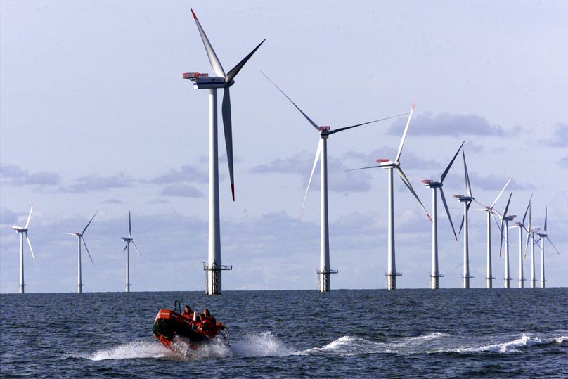 A speed boat passes along the over all 110 meters high offshore wind mills set up in the North Sea.