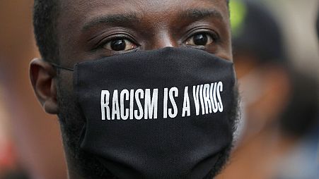 FILE - A protester wears a face mask in front of the US embassy, during the Black Lives Matter protest rally in London, Sunday, June 7, 2020.