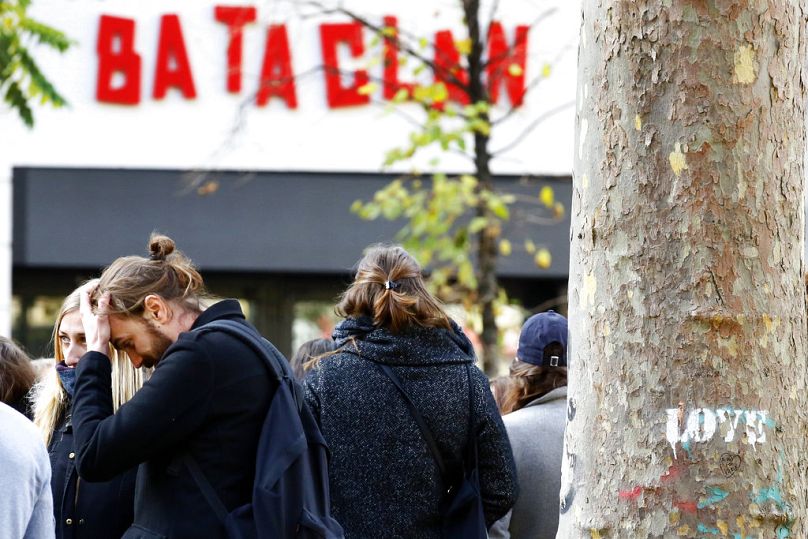 People stand in front of the Bataclan concert hall during a ceremony marking the second anniversary of the Paris attacks, Monday Nov.13 2017.