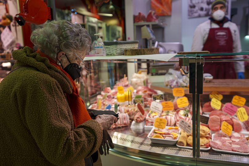 An elderly woman buys food in a market in Florence, Italy, Thursday, Feb. 17, 2022.