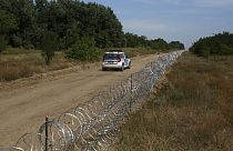 Egy magyar rendőrségi járőrkocsi halad el a határkerítés egy szakasza mellett a szerb-magyar határon, a szerbiai Hajdukovóban.