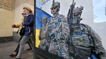 Pedestrians walk past a poster depicting Ukrainian servicemen and a slogan which reads "Bring the victory soon" in Kyiv, on 31 October