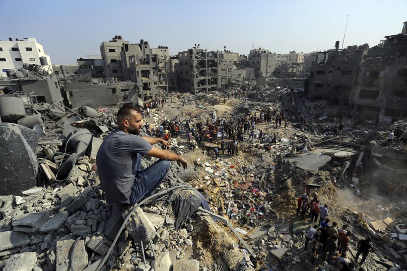 Un hombre sentado sobre los escombros mientras otros deambulan entre los edificios derruidos que fueron blanco de ataques israelíes en el campamento de refugiados de Jabaliya.
