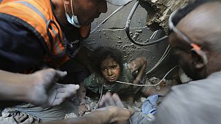 Palestinianos tentam tirar uma menina dos escombros de edifício destruído pelos ataques de Israel ao campo de refugiados de Jabalia, na Faixa de Gaza