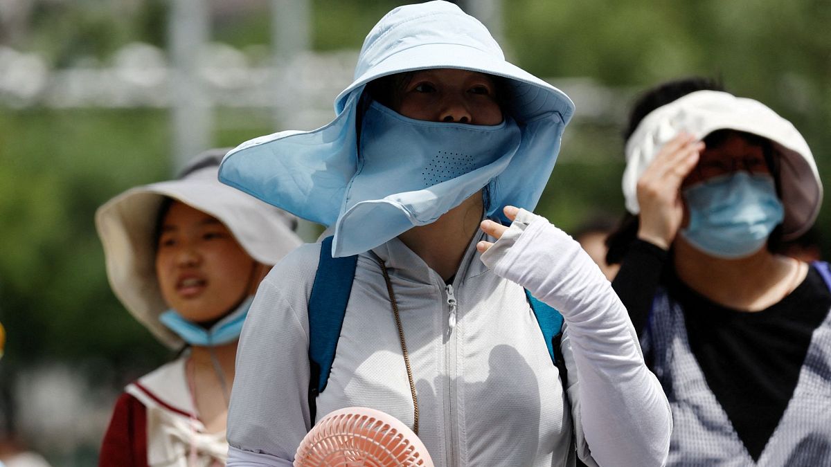 People wearing sun protection gear during a heatwave walk on a street in Beijing, China, 1 July 2023. 