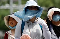 People wearing sun protection gear during a heatwave walk on a street in Beijing, China, 1 July 2023. 
