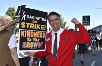 Actor Walt Keller dressed as Mister Rogers carries a sign on the picket line outside Universal Studios on Friday, Aug. 4, 2023, in Universal City, Calif.