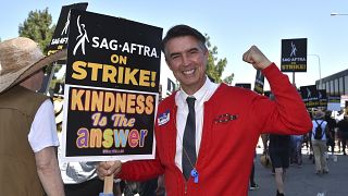 Actor Walt Keller dressed as Mister Rogers carries a sign on the picket line outside Universal Studios on Friday, Aug. 4, 2023, in Universal City, Calif.