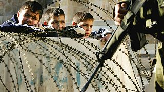Batı Şeria'nın El Halil kentinde bir İsrail askeri ve tel örgülerin hemen diğer tarafında duran Filistinli okul çocukları (arşiv)