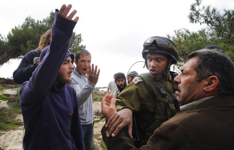 Batı Şeria'nın el Halil kentinde Yahudi yerleşimciler (solda) Filistinli bir kişiye bağırırken İsrail askeri araya giriyor (arşiv)