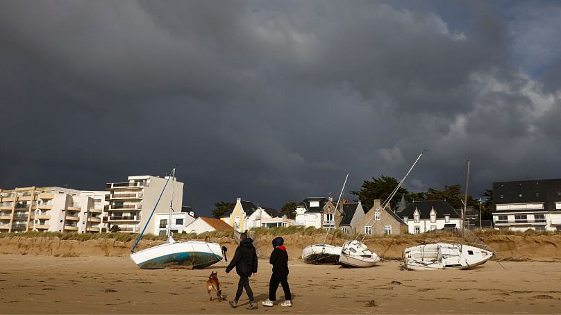 A couple walk their dog by washed ashore boats on the beach of Pornichet, Brittany, Thursday, Nov. 2, 2023.