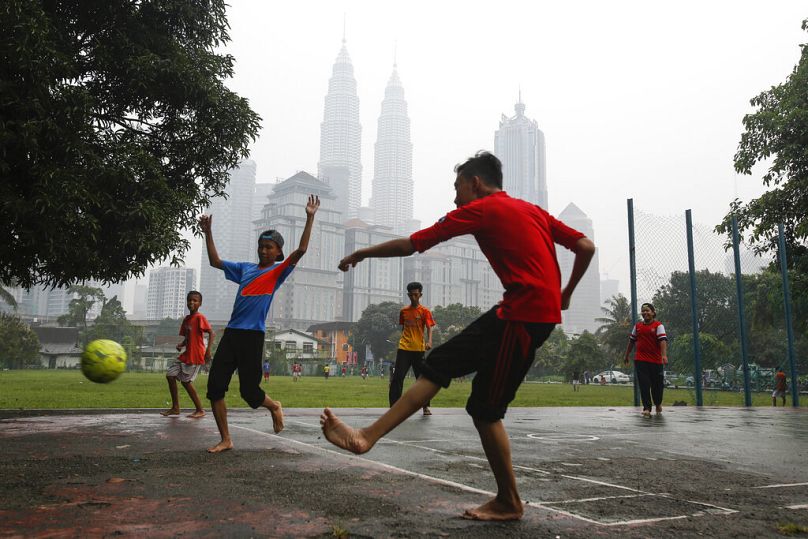 Young Malaysian plays soccer against Malaysia's landmark building Petronas Twin Towers, centre, shrouded with haze in Kuala Lumpur, September 2015