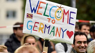  Хората приветстват бежанците с банер с надпис 