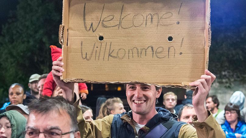 Мужчина держит картонку с лозунгом "Добро пожаловать" во время прибытия беженцев на железнодорожный вокзал в Заальфельде, центральная Германия, 2015 год.