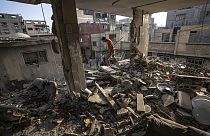Ein Mann steht in den Trümmern eines Wohnhauses. Im Hintergrund sind weitere zerstörte Gebäude zu sehen.
