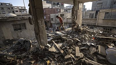 Ein Mann steht in den Trümmern eines Wohnhauses. Im Hintergrund sind weitere zerstörte Gebäude zu sehen.