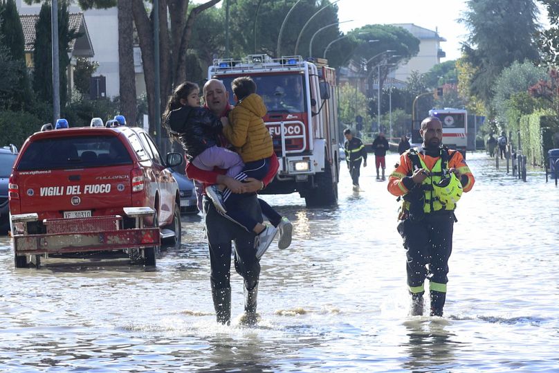 Un homme porte des enfants à travers les eaux de crue, les services d'urgence étant sur les lieux après de fortes pluies, en Toscane, Italie, en novembre 2023.