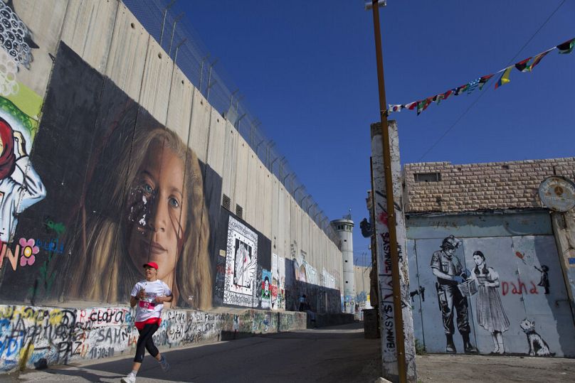 A runner passes by the Israeli separation barrier during the Palestine Marathon, in the West Bank city of Bethlehem, Friday, March 22, 2019.