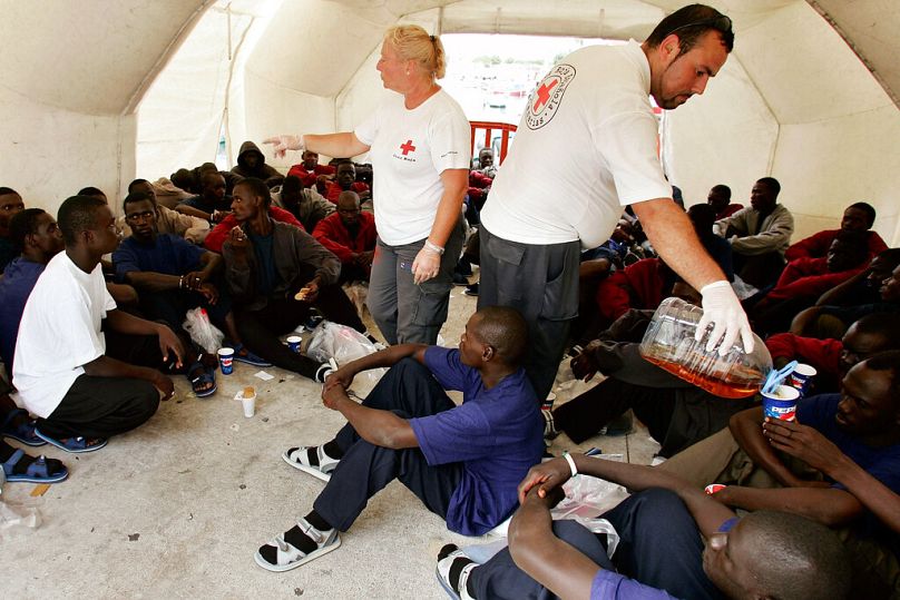 A Red Cross workers stand amid some of the 105 would-be immigrants in a tent after they arrived in the port of Los Cristianos on the Canary Island of Tenerife, Spain.